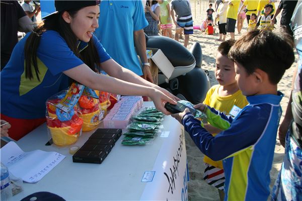 수협은행 ‘어촌체험 가족나들이’ 행사가 개최된 강원도 양양 하조대 해수욕장에서 행사 스탭이 참가한 어린이들에게 기념품을 전달하고 있다. 사진=수협은행 제공