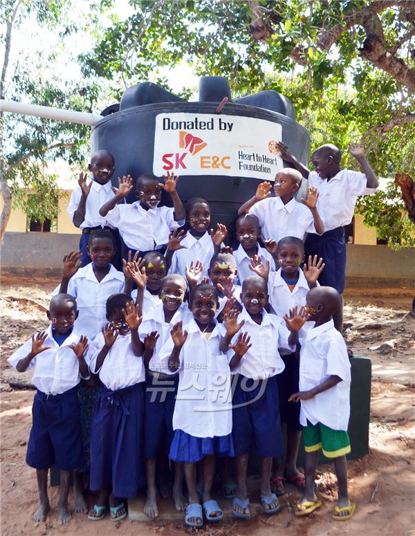 탄자니아 초등학교 학생들이 SK건설이 기부한 물탱크 앞에서 기념촬영을 하고 있다. 사진=SK건설 제공