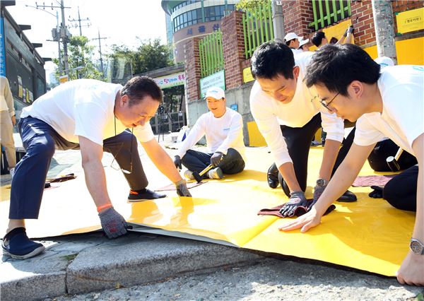 박용만 두산그룹 회장(왼쪽)이 14일 서울 중구 신당초등학교에서 임직원들과 함께 어린이들의 안전한 보행을 돕기 위한 안전지대인 옐로카펫을 부착한 후 잘 붙도록 고무망치로 두드리고 있다. 사진=두산 제공