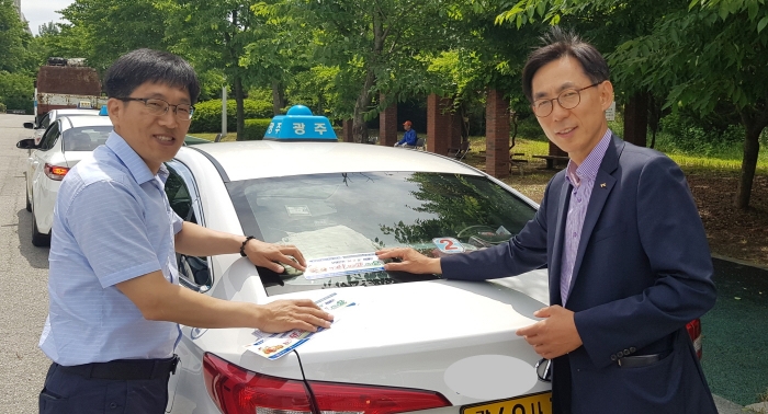 한국교통안전공단 광주전남본부 문재업 안전관리처장(사진 오른쪽)이 전국택시공제조합 광주지부와 함께 광주비엔날레주차장에서 광주 법인택시 외관에 ‘서고요 캠페인 스티커’를 부착하고 있다.