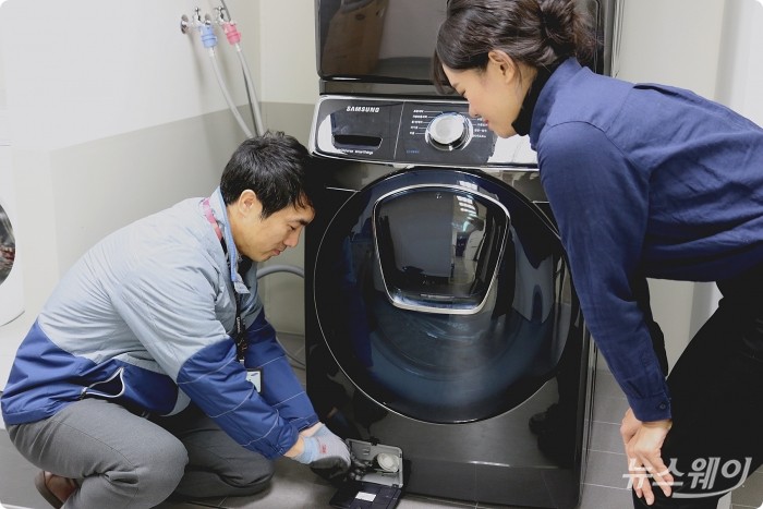 삼성전자서비스 수리 엔지니어가 출장 점검 서비스를 신청한 고객에게 플러스 원 케어 서비스의 일환으로 드럼세탁기 배수펌프 잔수 제거 방법을 설명하고 있는 모습. 사진=삼성전자서비스 제공