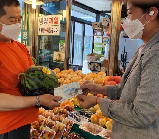여성가족과-캄보디아 출신 결혼이민자가 성남 중앙시장에서 성남사랑상품권으로 수박을 사고 있다.