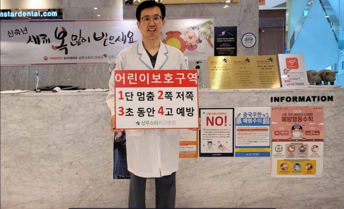 상무스타치과병원 김운규 원장이 9일 ‘1단 멈춤, 2쪽 저쪽, 3초 동안, 4고 예방’이라는 피켓을 들고 ‘어린이 교통안전 릴레이 챌린지’ 캠페인에 참여하고 있다.