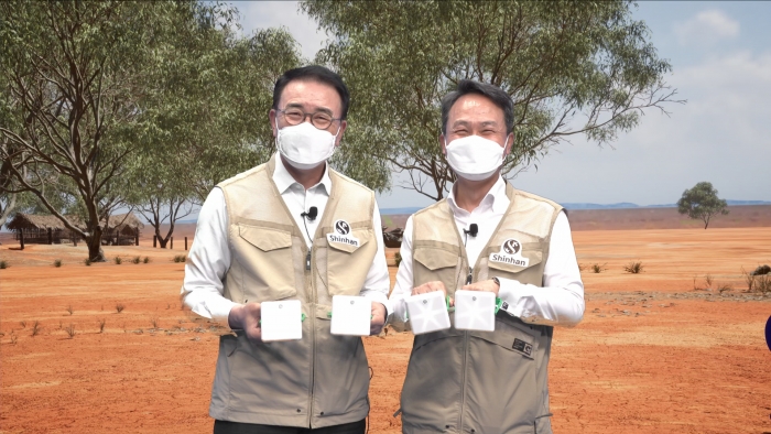 신한금융그룹은 15일 2021 Global One Shinhan 자원봉사 대축제의 시작을 알리는 태양광 랜턴 만들기 봉사활동을 언택트 방식으로 진행했다. 신한금융그룹 조용병 회장(사진 왼쪽)과 신한은행 진옥동 은행장이 신한은행 디지털 방송국에 구축한 AR 스튜디오에서 증강현실을 활용해 구현한 아프리카 마을 현장을 배경으로 기념 촬영을 하고 있다. 사진=신한금융그룹 제공