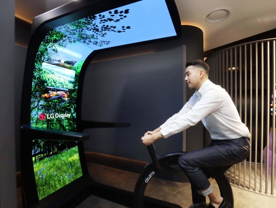 LG디스플레이 직원이 대형 OLED 스크린에 운동기구를 결합한 콘셉트의 플렉서블(Flexible) OLED 솔루션 ‘버추얼 라이드(Virtual Ride)’를 체험하고 있다. 사진=LG디스플레이
